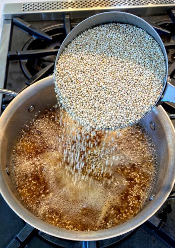 pouring 2 cups quinoa into pot of boiling broth