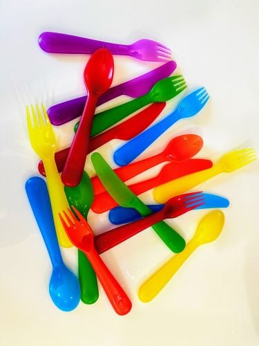 rainbow, plastic IKEA flatware spread out on white table