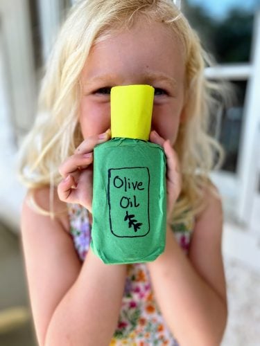 Child holding completed olive oil bottle craft with "Olive Oil" logo