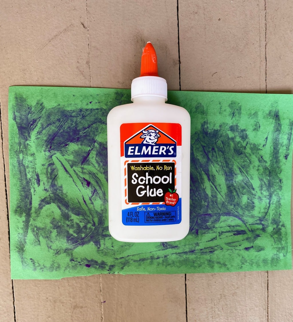 laying empty glue bottle onto green paper covered with glue