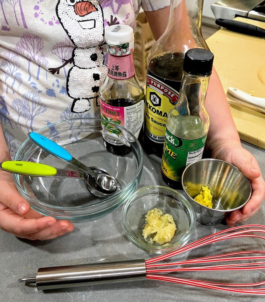 child holding ingredients for cauliflower rice sauce, plus measuring devices, whisk and bowl