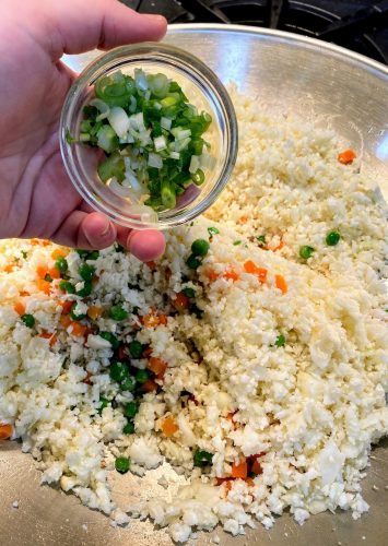 adding chopped scallion to cauliflower rice in wok
