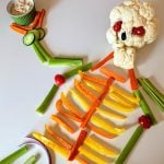 skeleton made of vegetables, with a cauliflower skull, holding a bowl of dip
