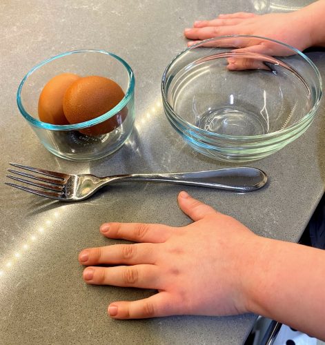 2 eggs, bowl, fork and child's hands on counter