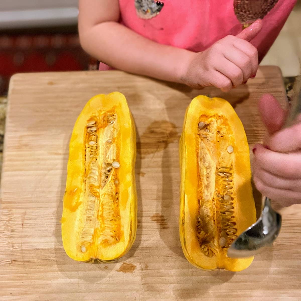 scooping seeds and guts out of delicata squash in order to bake