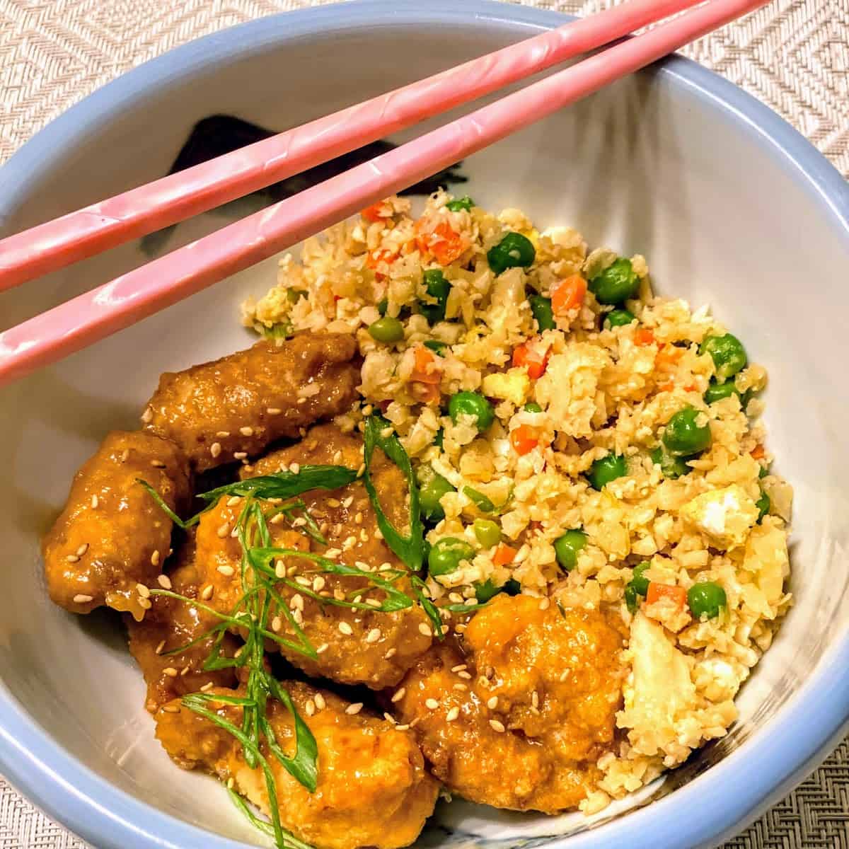 Cauliflower Egg Fried Rice with Orange Sesame Chicken in a Bowl with Pink Chopsticks