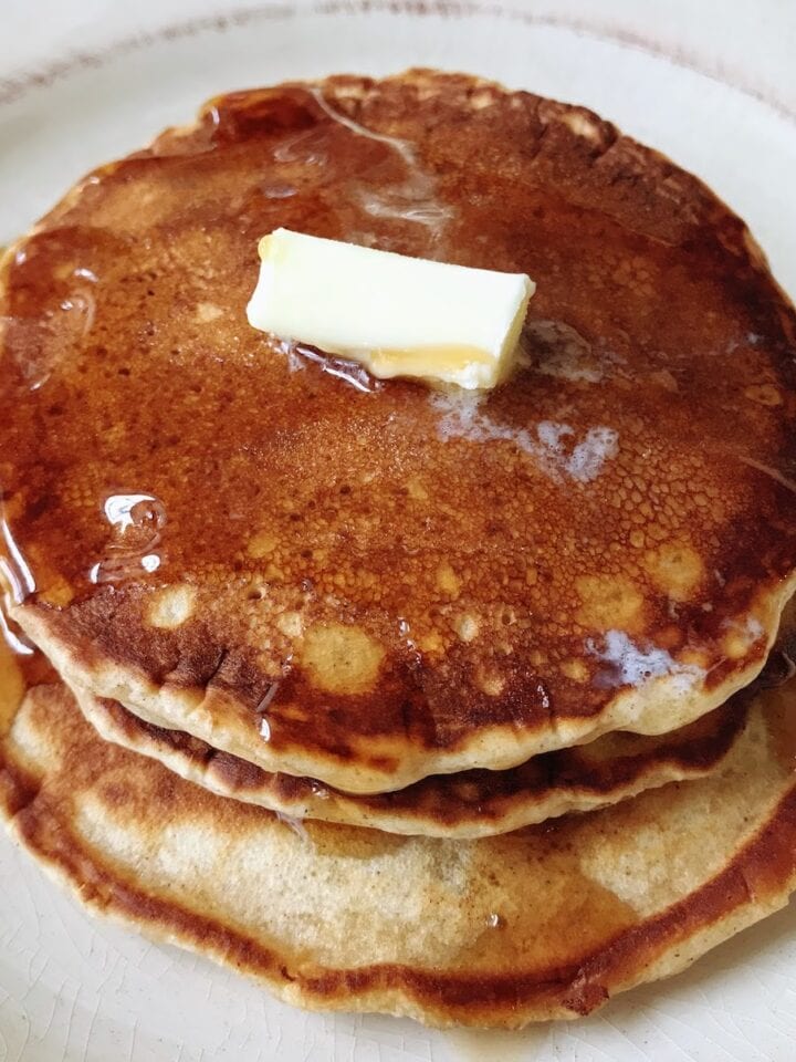 three stacked pancakes with butter and syrup