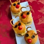 Four reindeer sliders on a white plate with Rudolph noses made from tomatoes.