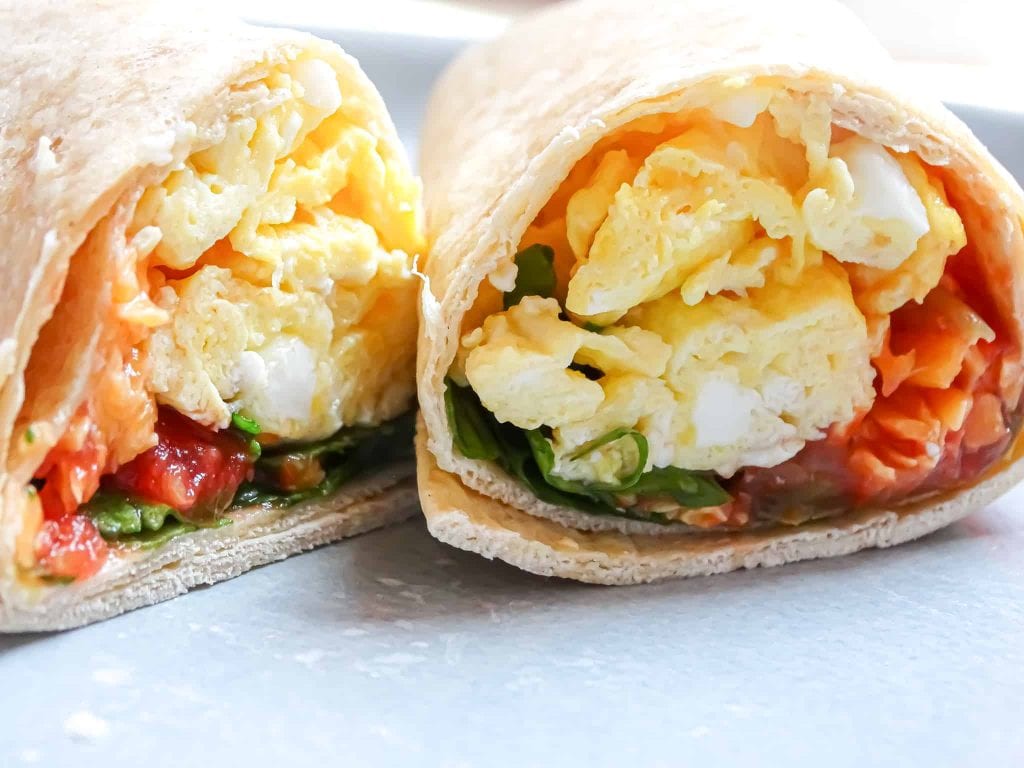 breakfast burrito cut in half with tomatoes and greens