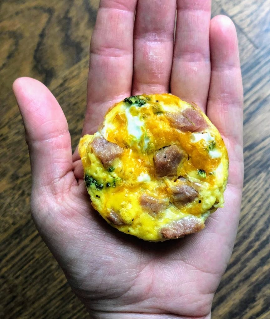 hand holding mini egg bite with ham, broccoli and cheese