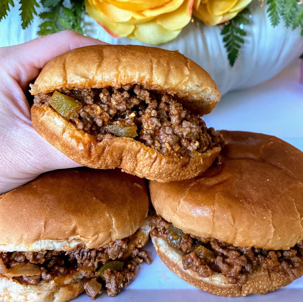 hand holding sloppy joes and two sandwiches resting on a plate