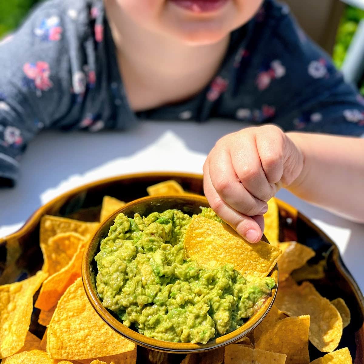child dipping a tortilla chip into guacamole