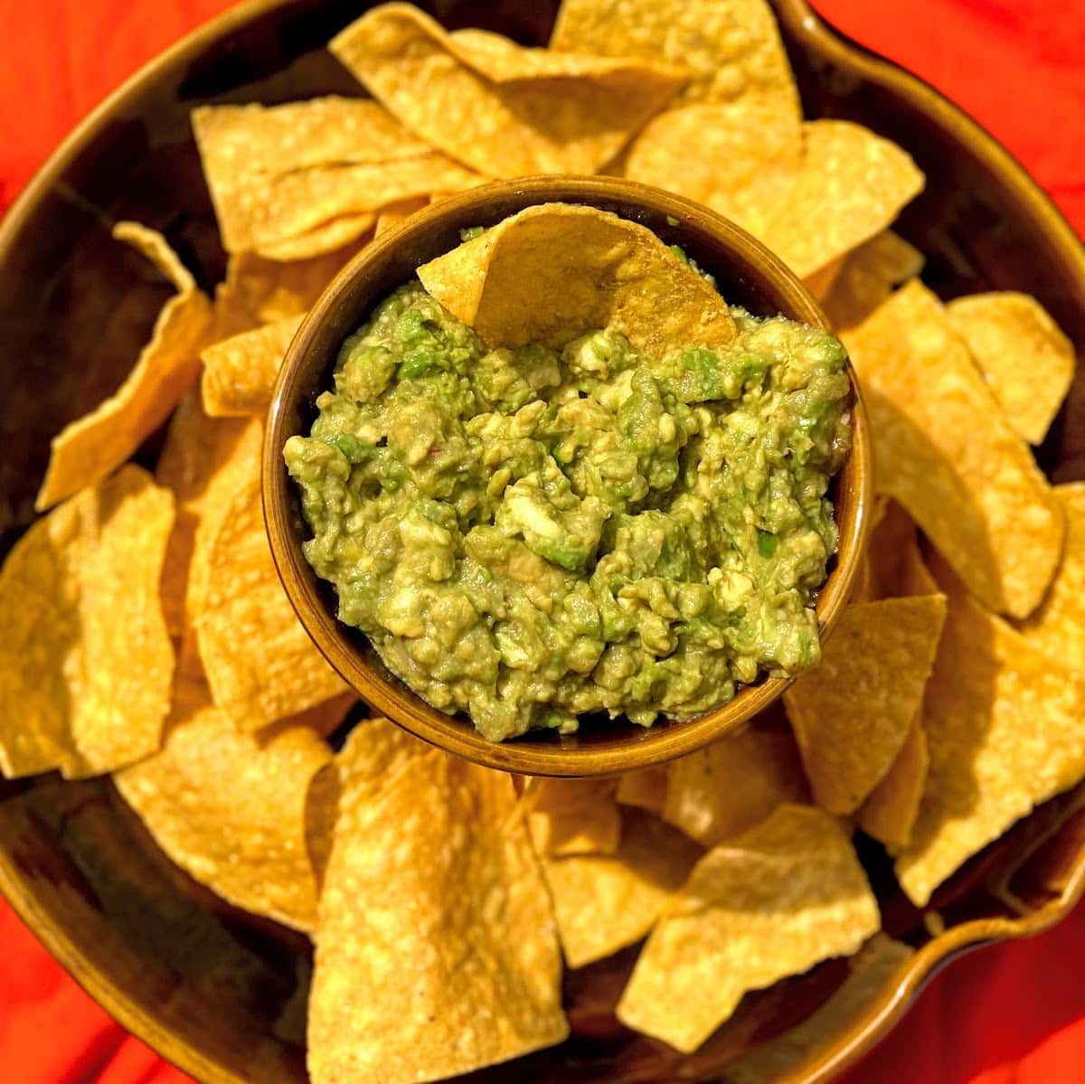 guacamole and tortilla chips in brown bowl on orange tablecloth