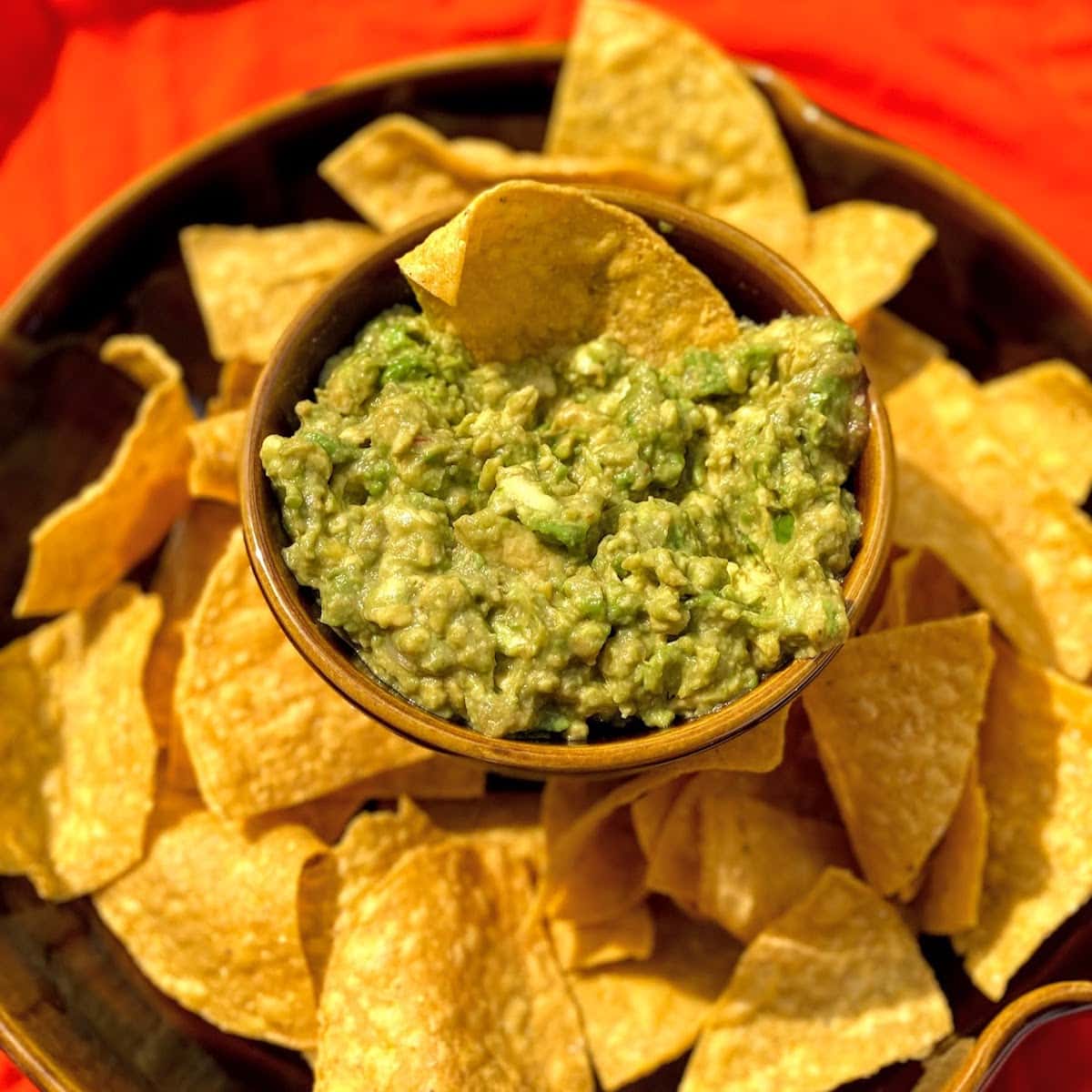 brown bowl filled with tortilla chips and guacamole dip