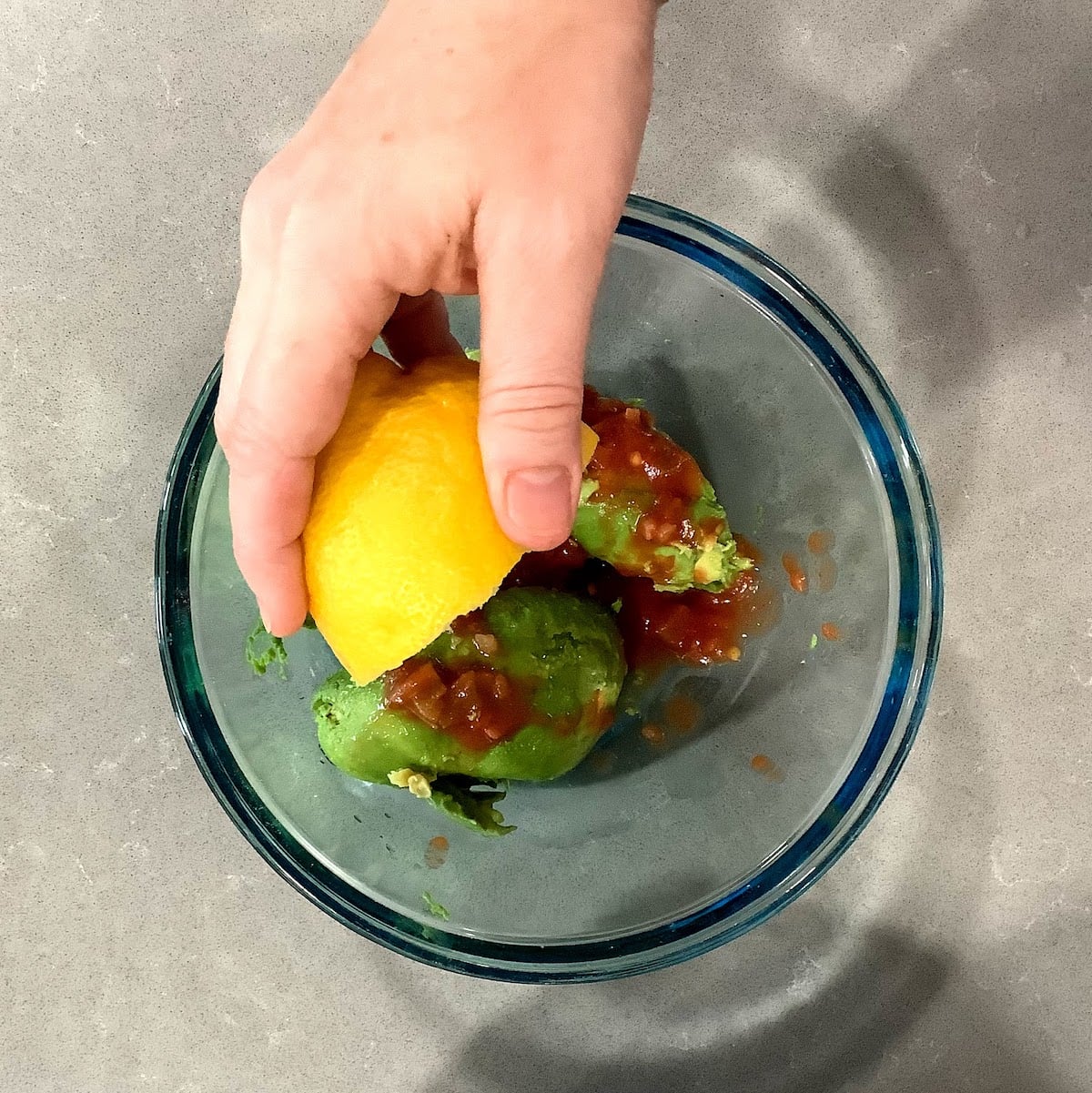 adding lemon juice to bowl to make guacamole