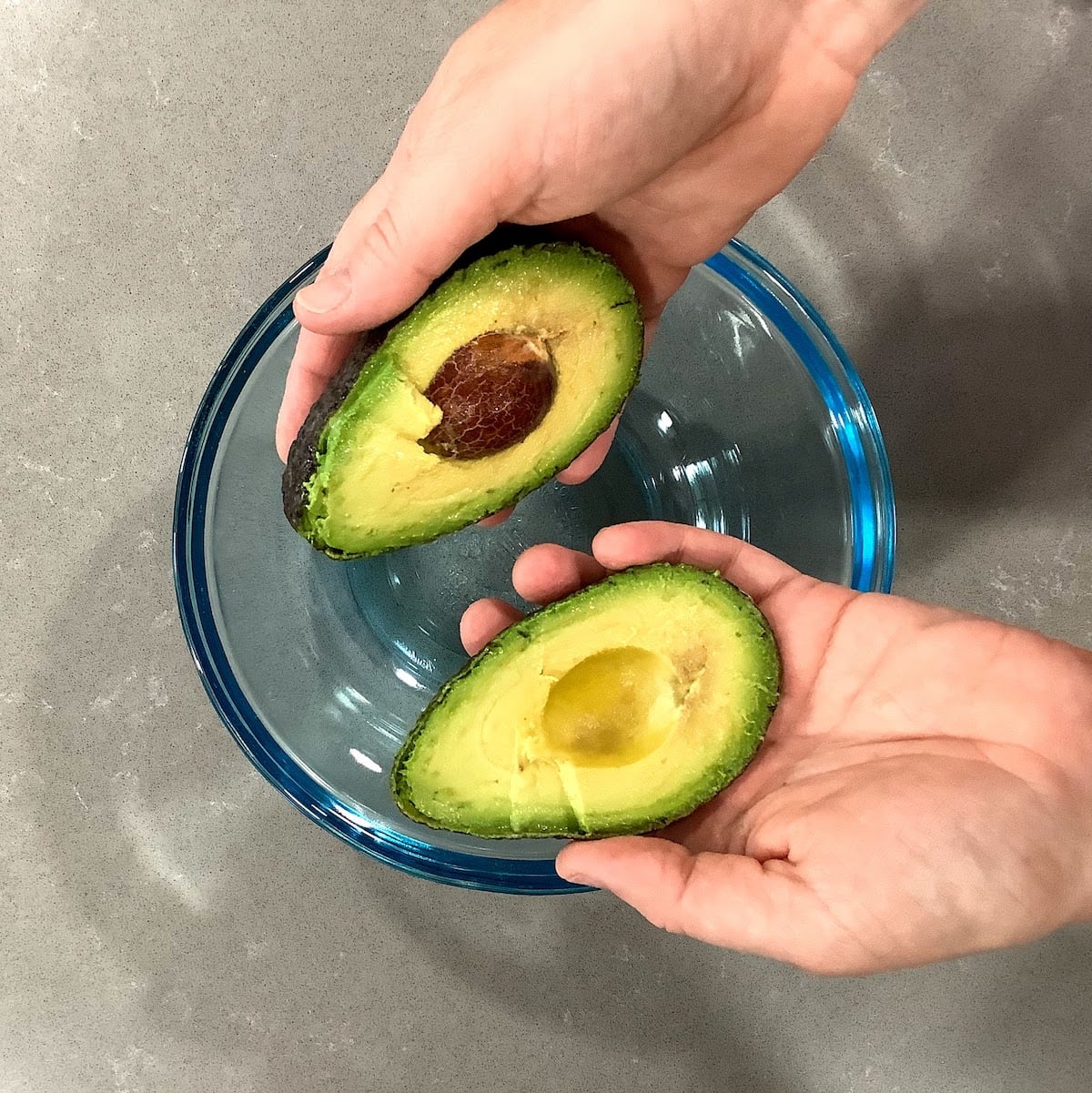 hands holding cut-open avocado over a bowl
