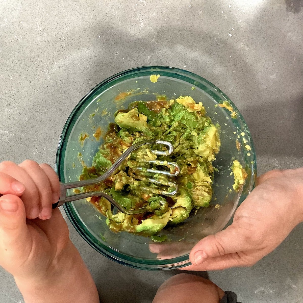 mixing guacamole in bowl using potato masher