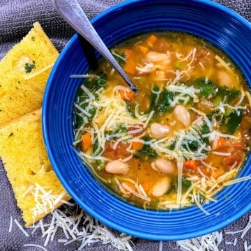 blue bowl of white bean soup with parmesan cheese and garlic bread