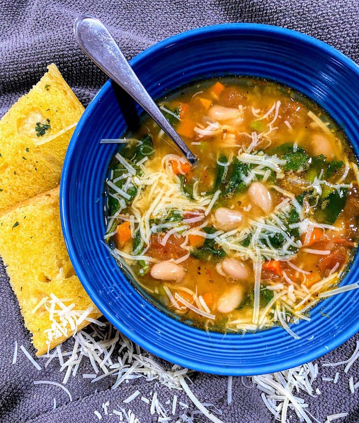 blue bowl of cannellini bean soup with parmesan cheese and garlic bread