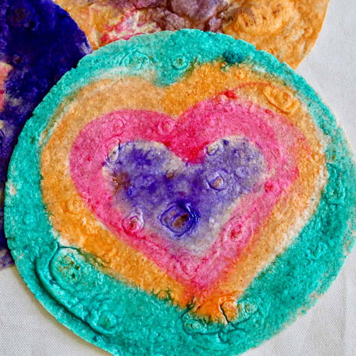 Tortillas colored with purple, pink, orange and teal food coloring in the shape of hearts. 