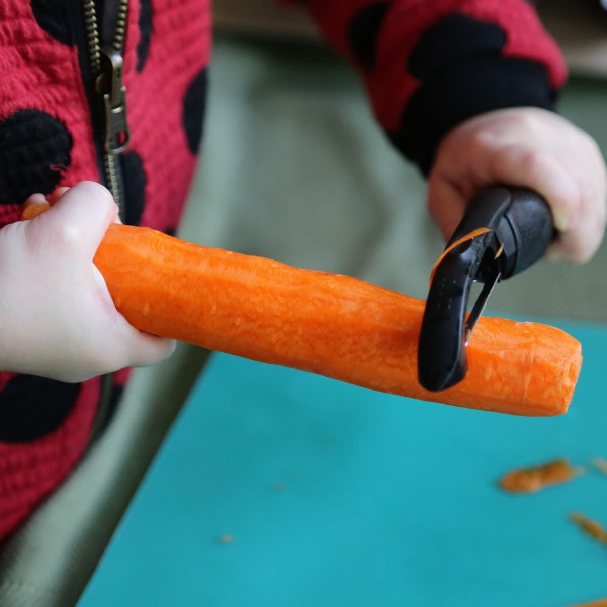 child peeling a carrot over a teal cutting board