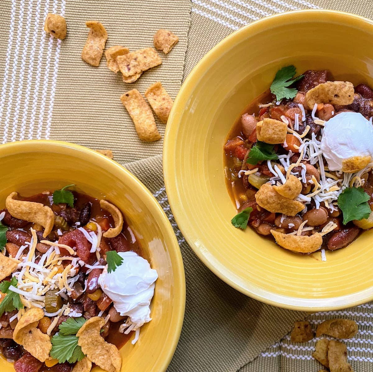 two yellow bowls of chili with corn chips and sour cream and cheese