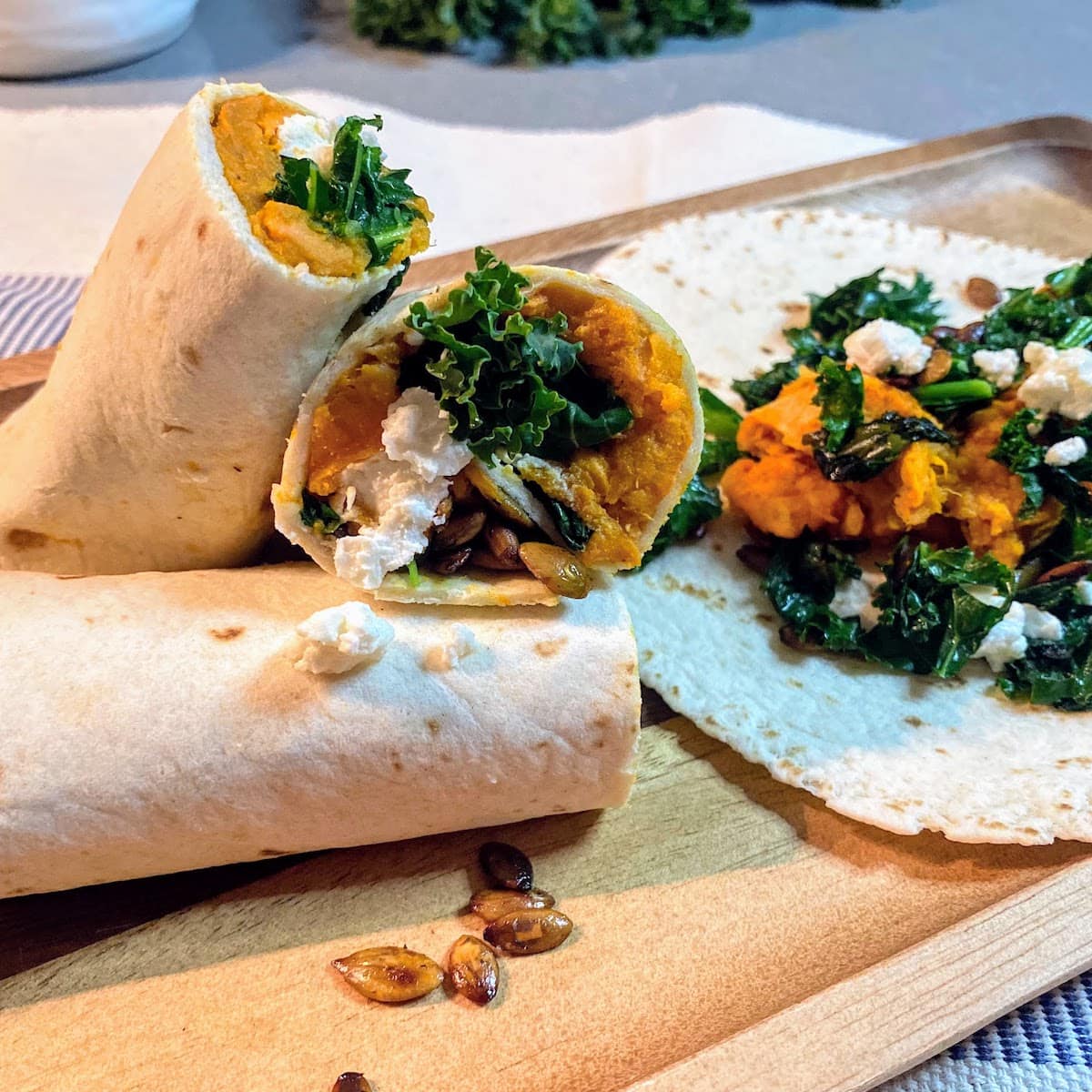 wrapped tortillas with sweet potatoes, kale and feta on wooden platter