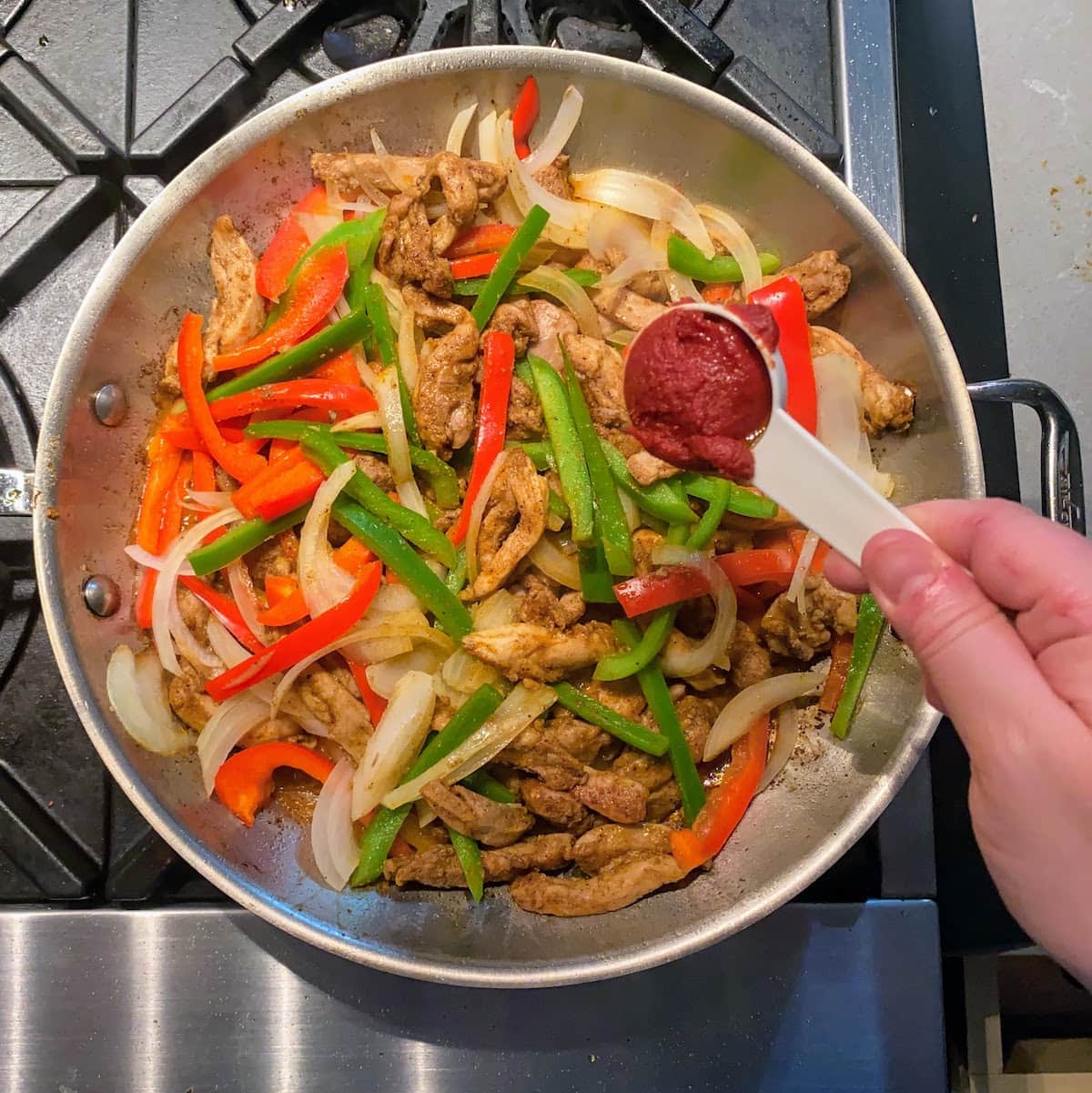 adding tomato paste to hot pan of fajita chicken and veggies