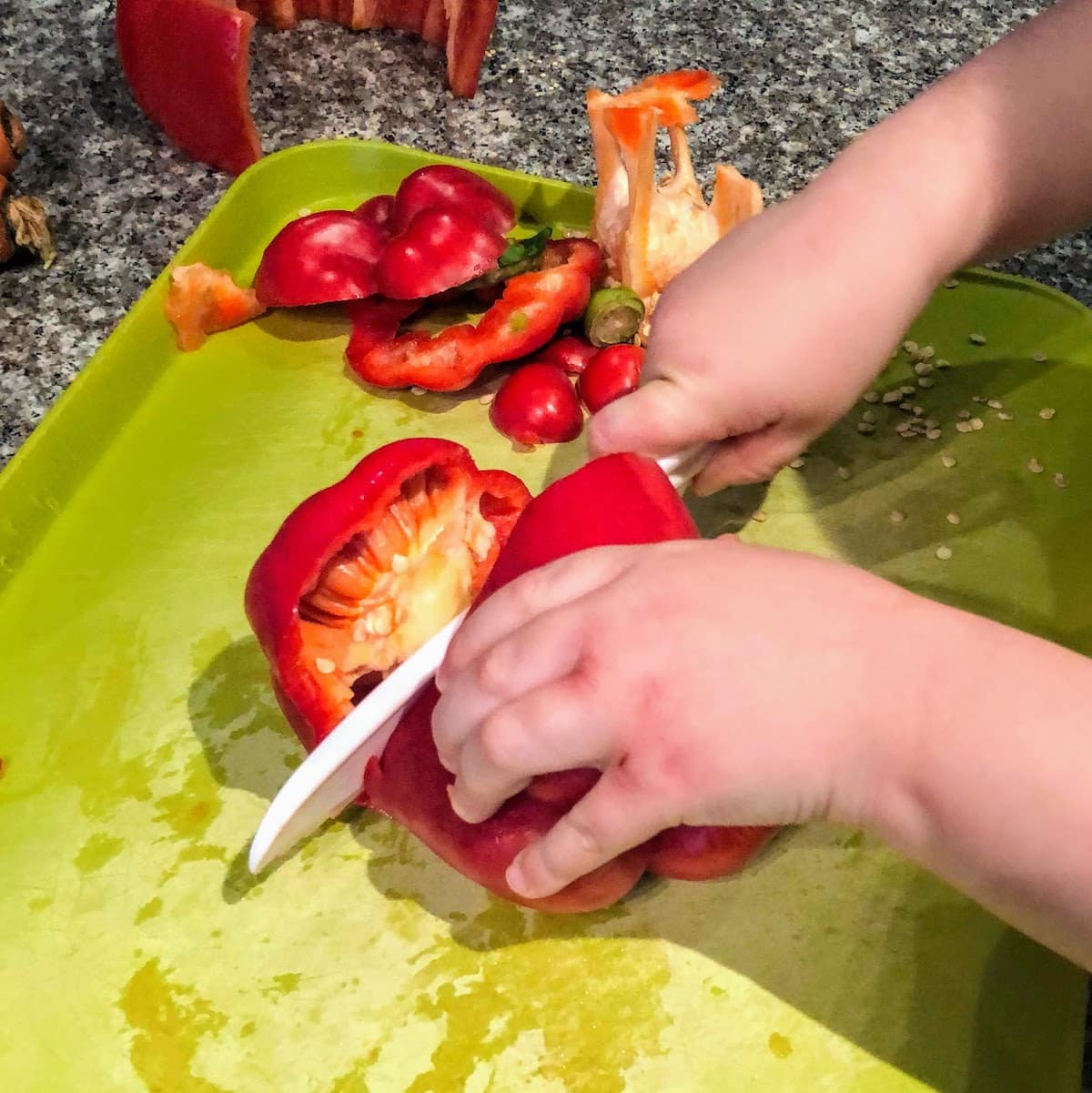 child cutting red bell pepper on green cutting board