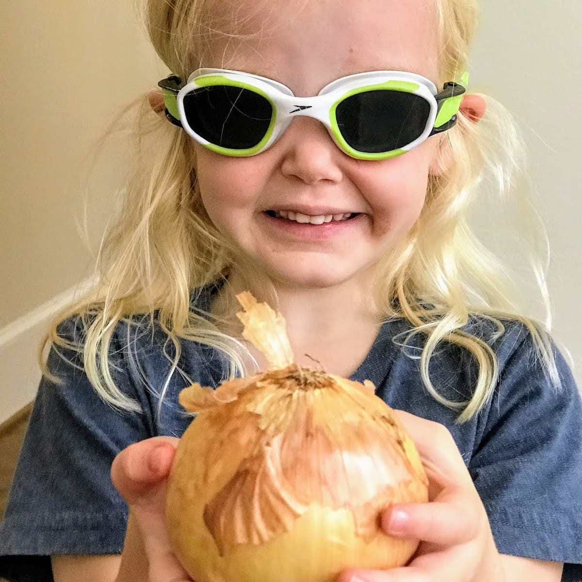 blonde child holding onion and wearing swim goggles