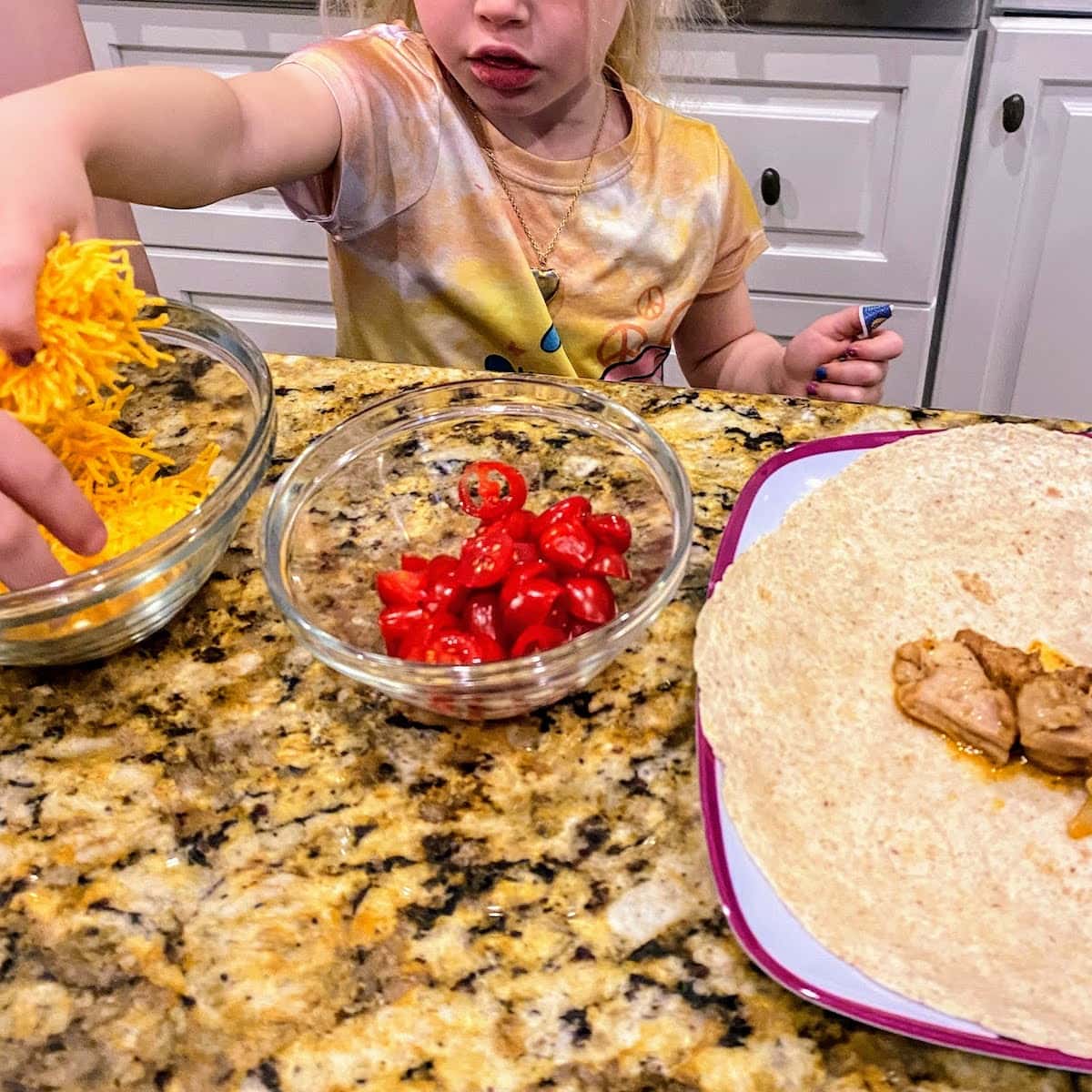 child putting cheese and tomatoes onto a chicken taco