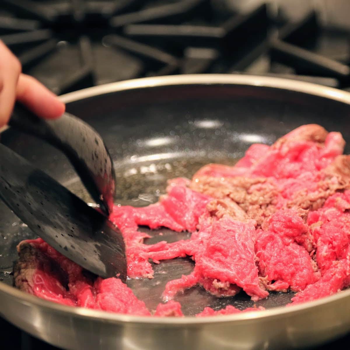 spoon and spatula breaking apart meat as it cooks in pan