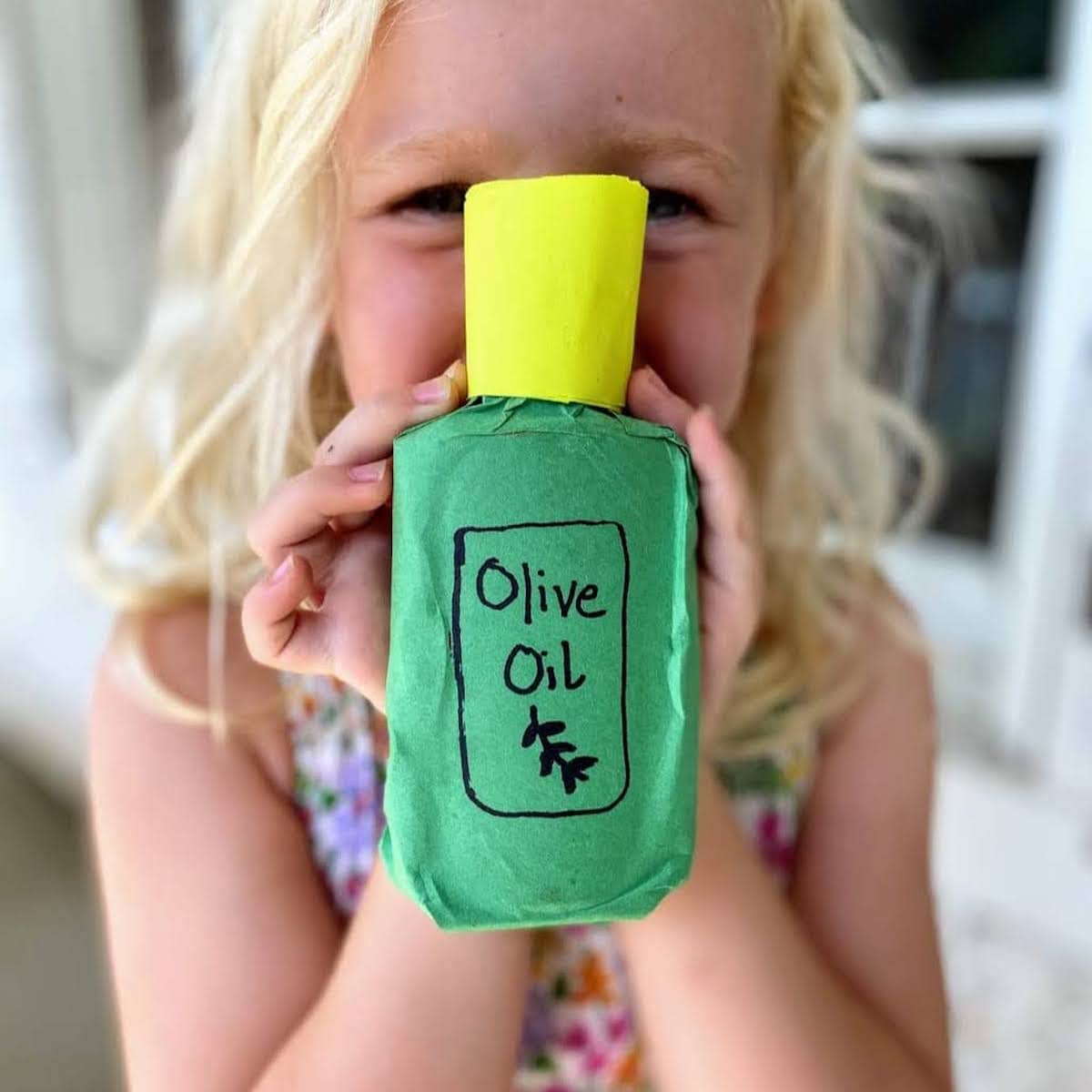 Child holding completed olive oil bottle craft with "Olive Oil" logo