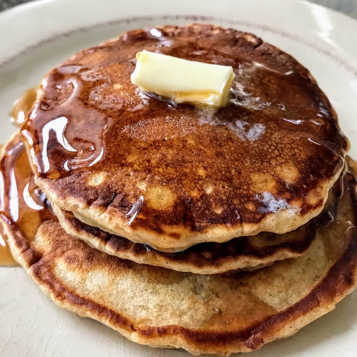 stacked cinnamon pancakes with butter and syrup on plate