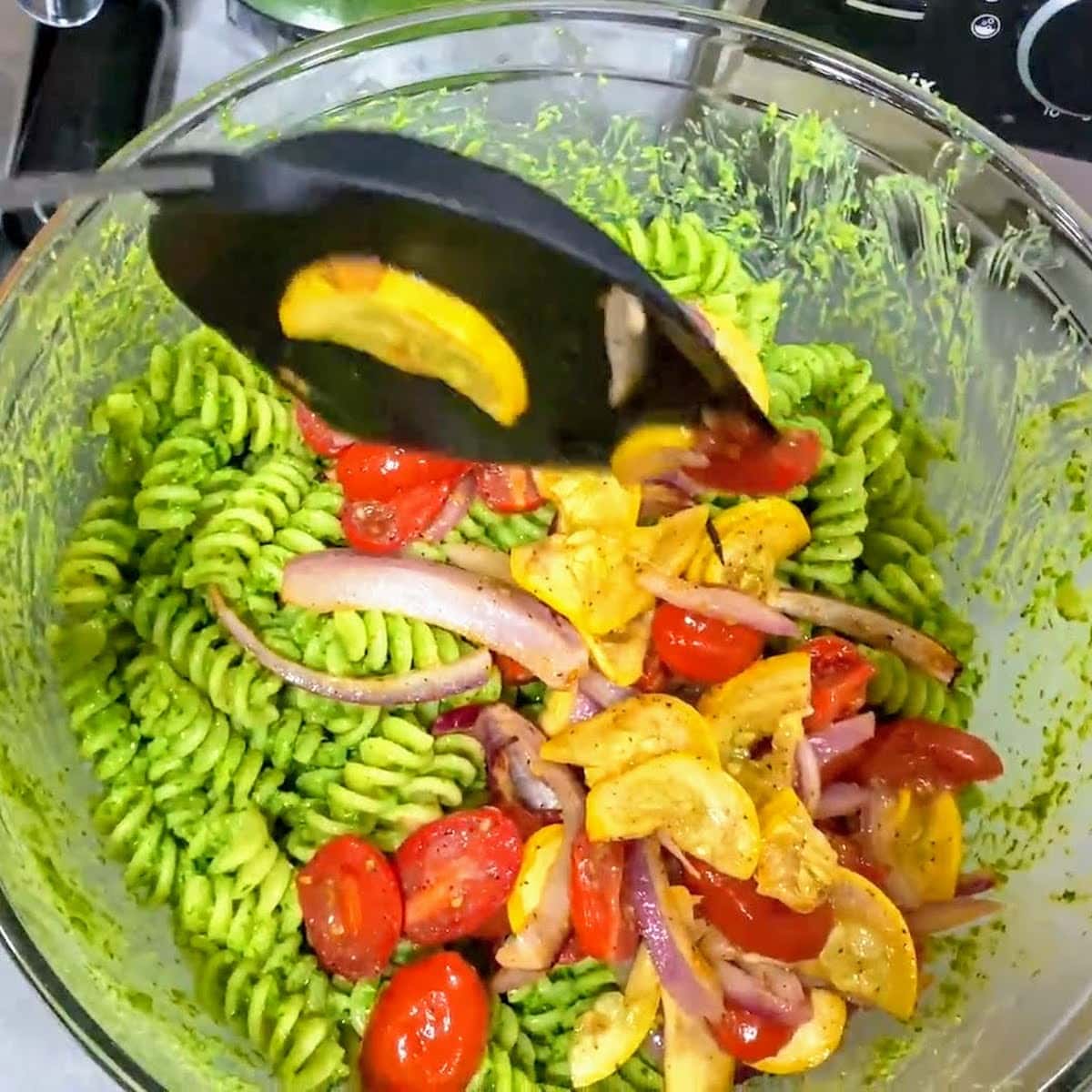 spatula adding roasted veggies to bowl of pesto pasta