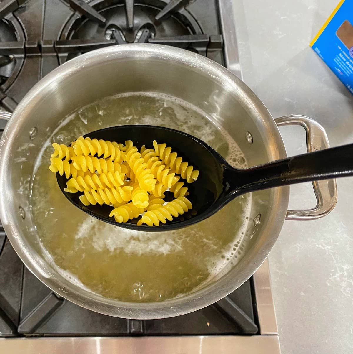 slotted black spoon holding fusilli pasta over pot of boiling water