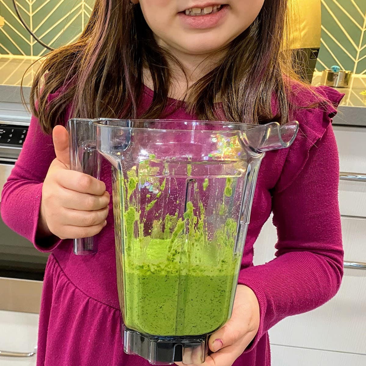 girl holding Vitamix container of blended pesto sauce