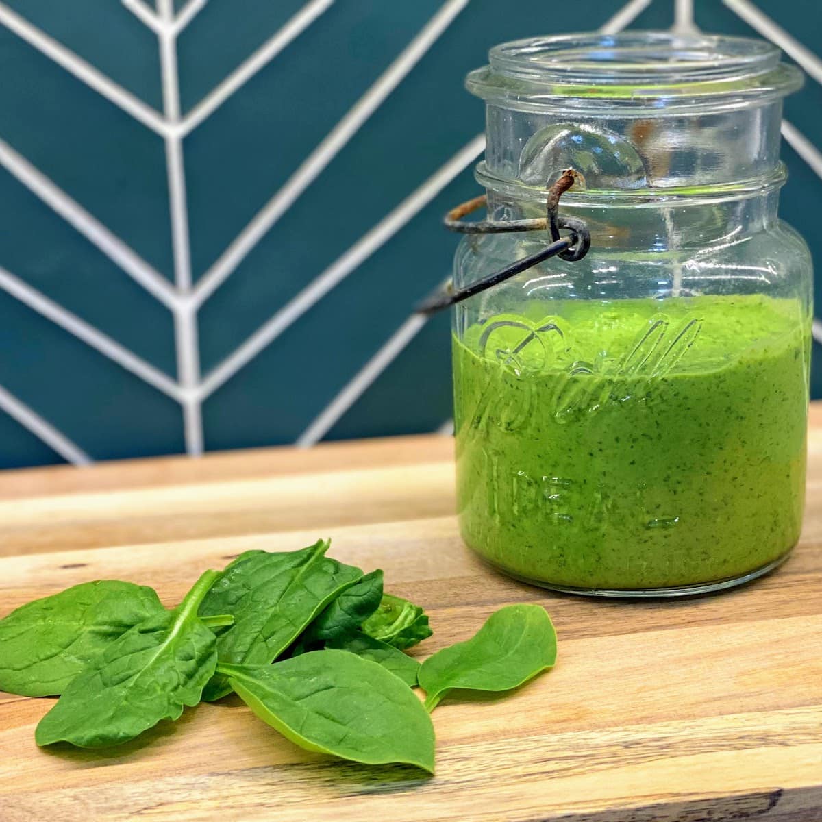 old Ball jar of green pesto sitting next to fresh greens on wooden board