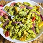 hand holding fork and bowl of pasta with roasted veggies and pesto sauce