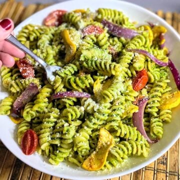 hand holding fork and bowl of pasta with roasted veggies and pesto sauce