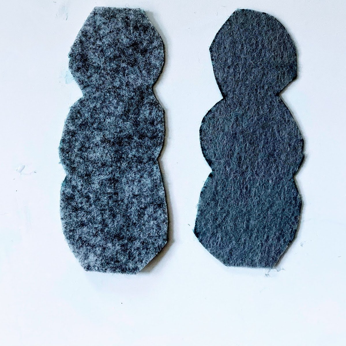 two gray cutouts of snowmen from felt 