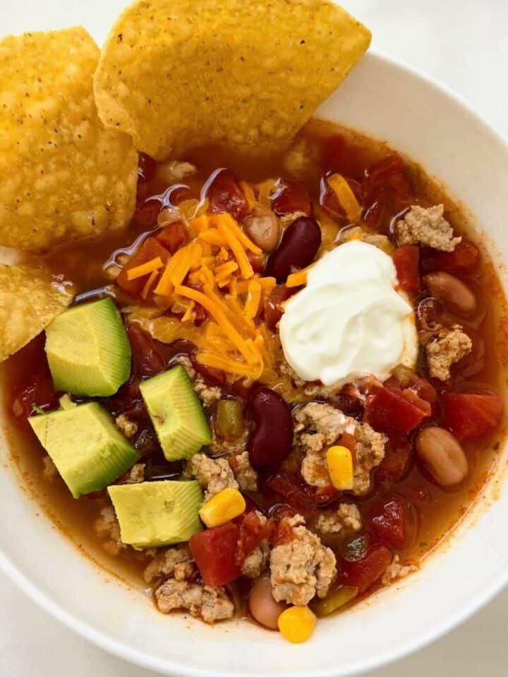 A bowl of taco soup with ranch topped with chips, avocado, cheese and sour cream.