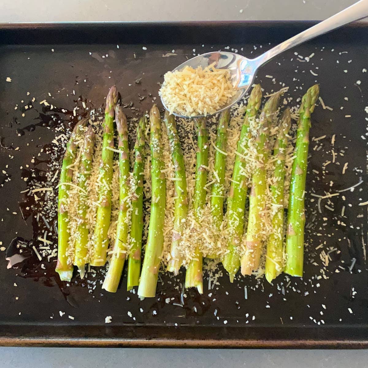 pouring parmesan panko mix over the asparagus in pan