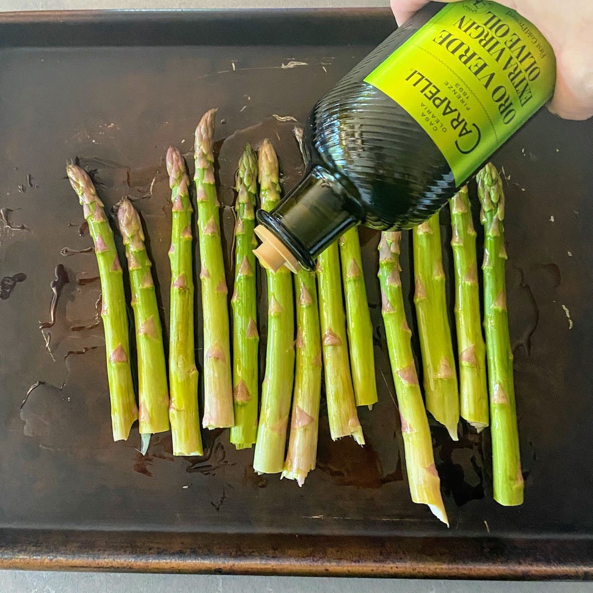 hand pouring olive oil onto baking sheet asparagus