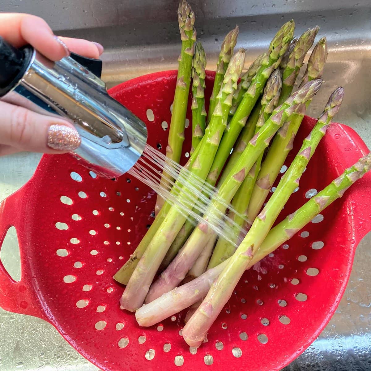 rinsing asparagus in red colander in sink