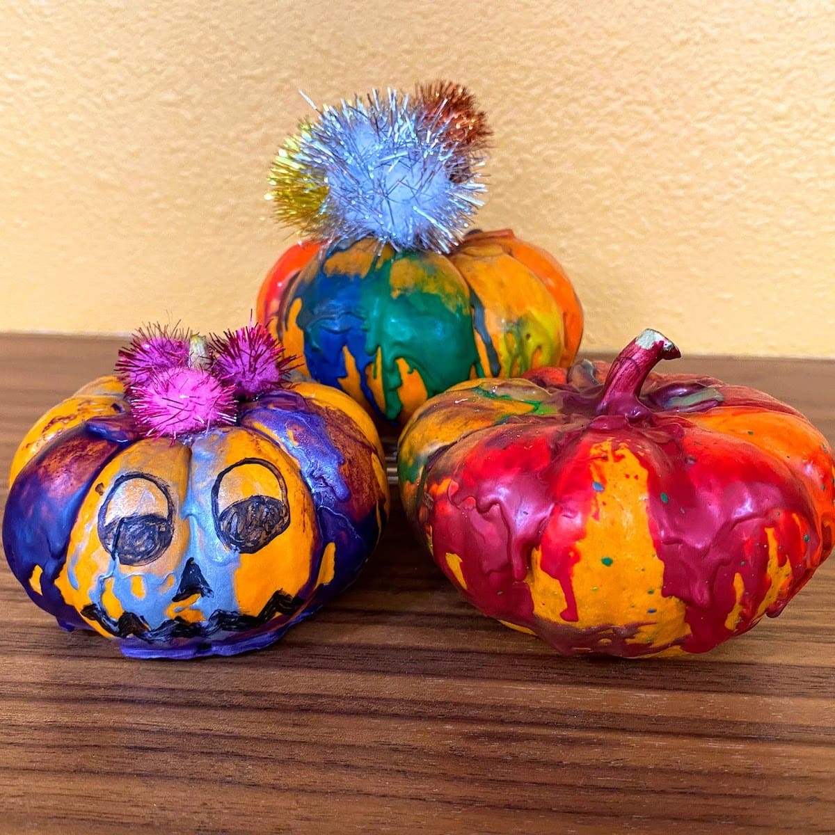 three mini pumpkins with melted rainbow crayons