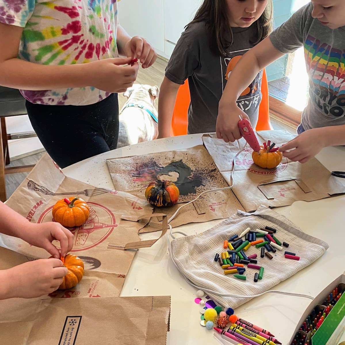 kids gluing crayons to pumpkins at kitchen table