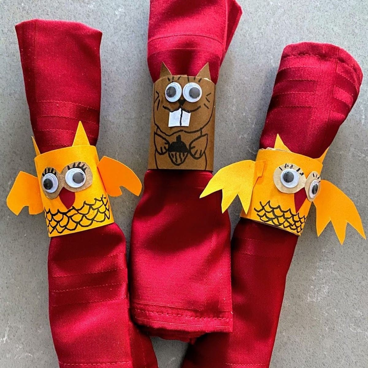 three napkin rings of owls and a squirrel holding red napkins