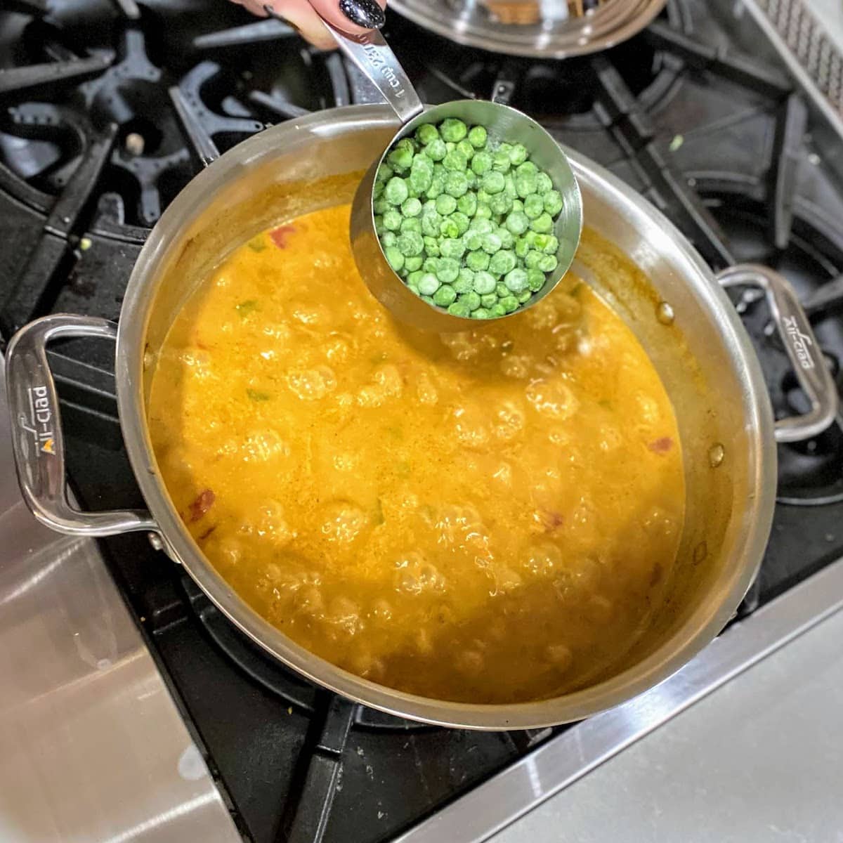 adding frozen peas to pot of coconut curry