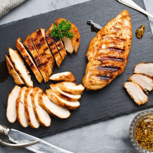 sliced chicken on slate serving platter with mustard and utensils